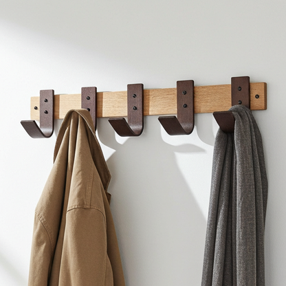 Wooden wall hook with walnut hooks holding a brown jacket and gray coat against a white wall.